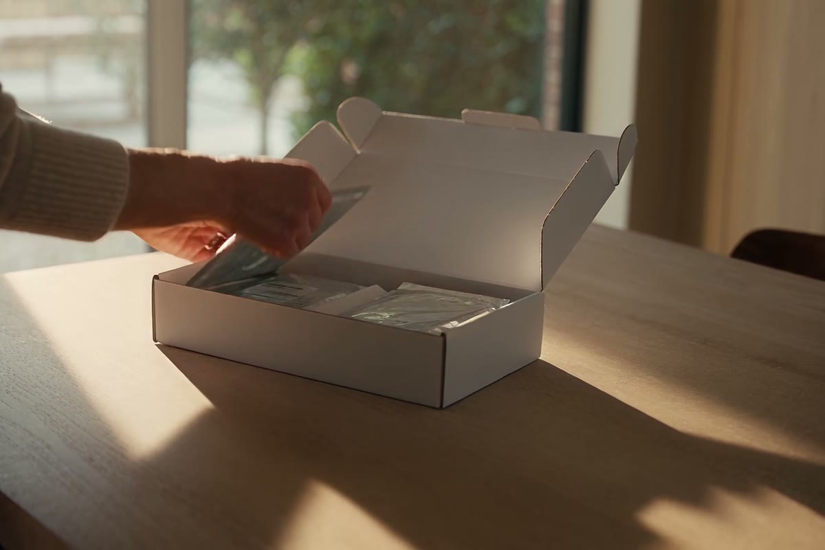 Hands lifting an instruction card from a plain white sample kit on a kitchen table.